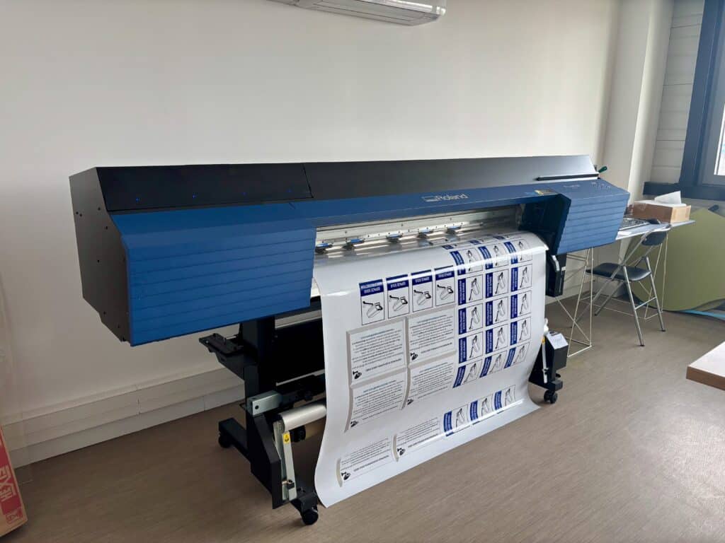Impression Roland : signalisation grand format autocollants Imprimante grand format Roland TrueVIS produisant des autocollants "ESPACE SOUS VIDEOPROTECTION" avec pictogramme de caméra de surveillance.